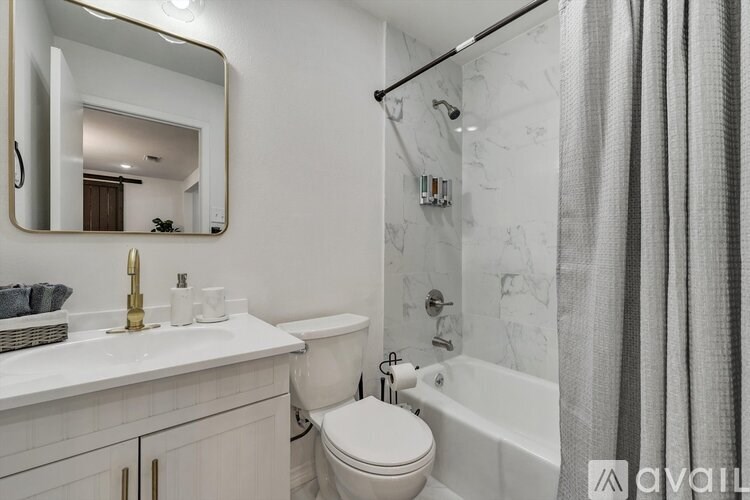 A bathroom with a white toilet, a sink with a gold faucet, and a shower with a grey curtain.