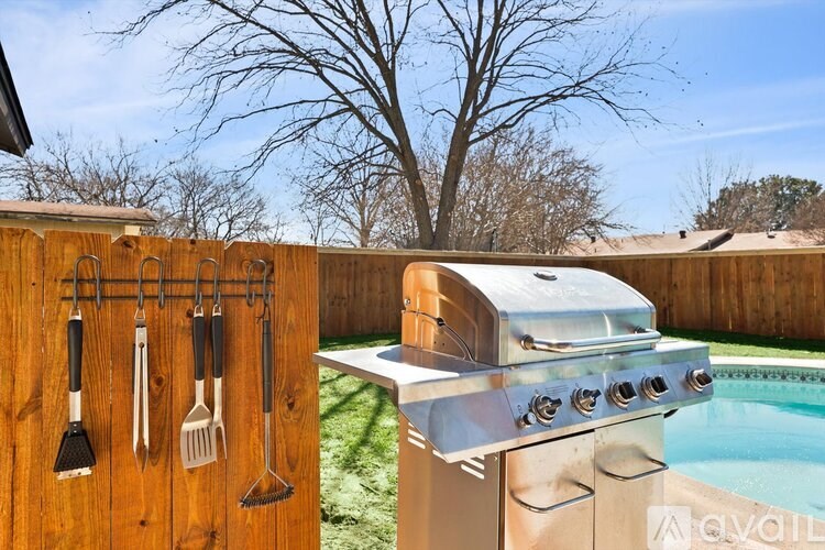 A grill with utensils hanging on a wooden fence next to a pool.