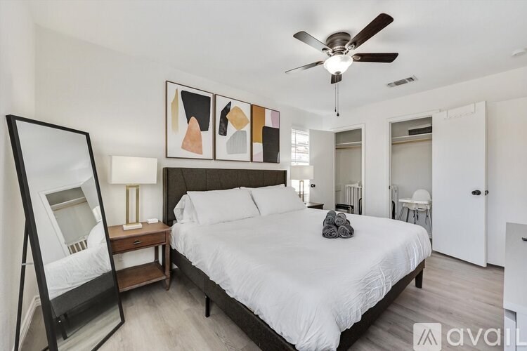 A bedroom with a large bed, a ceiling fan, and a painting on the wall.
