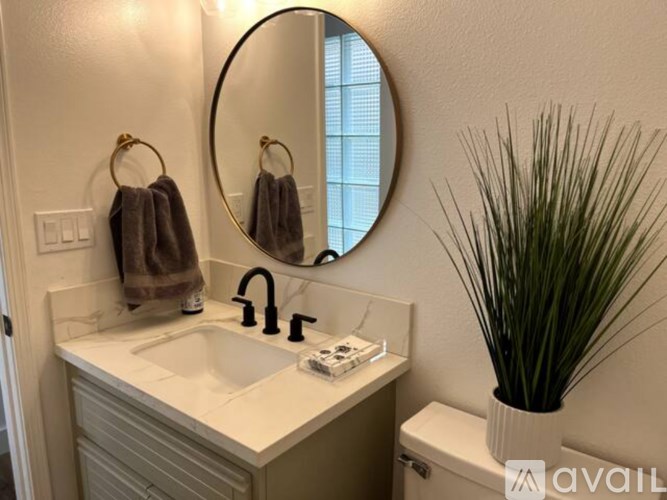 A bathroom with a round mirror, a sink, and a plant.