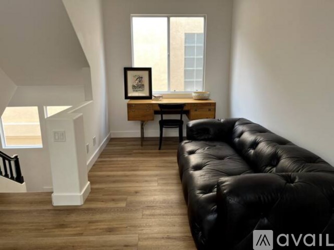 A black leather sofa sits in a room with wooden floors and white walls.