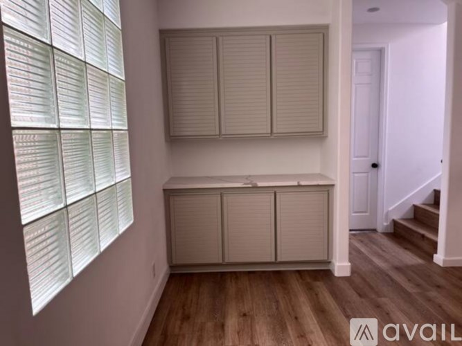 A room with wooden floors, a window with blinds, and a cabinet with a countertop.