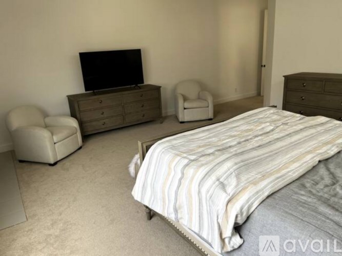 A bedroom with a large bed, a chair, a dresser, and a television.