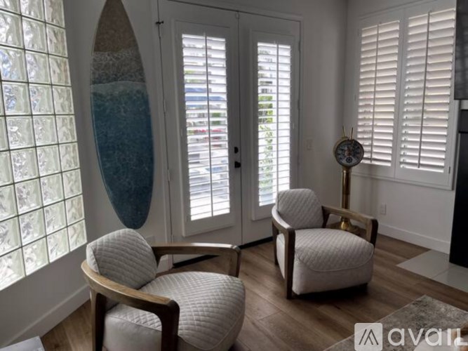 A room with a surfboard on the wall and two chairs.