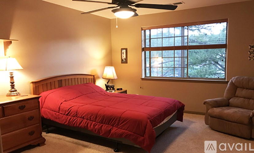 A bedroom with a red bedspread and a ceiling fan.