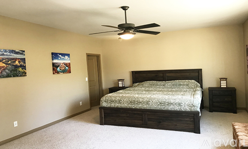 A bedroom with a bed, a ceiling fan, and two pictures on the wall.