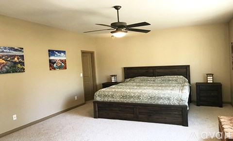 A bedroom with a bed, a ceiling fan, and two pictures on the wall.