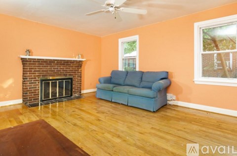 A blue couch sits in a living room with a brick fireplace and a ceiling fan.