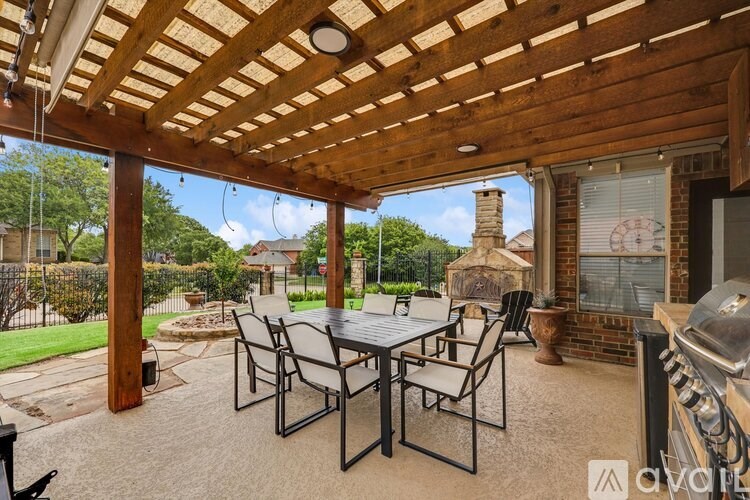 A patio with a table and chairs is covered by a wooden roof.