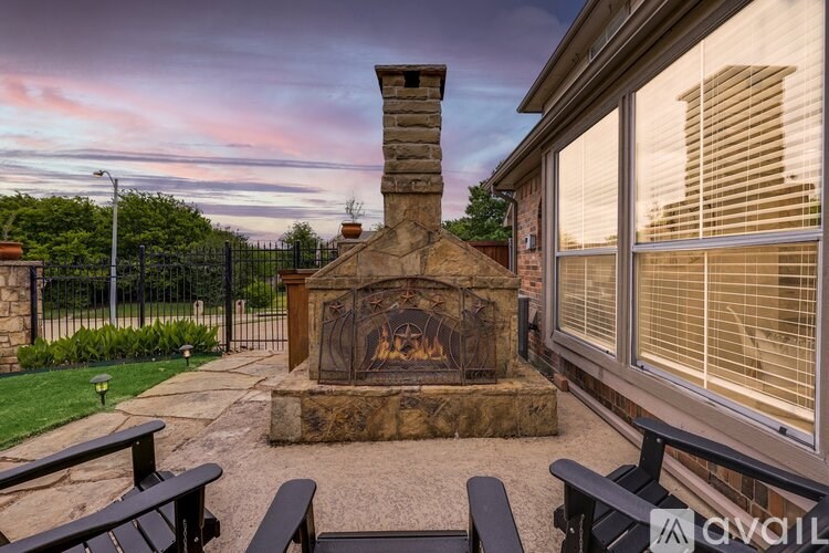 A stone fireplace is the centerpiece of a patio with a bench and a fence in the background.