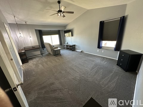 A living room with a grey carpet and a ceiling fan.