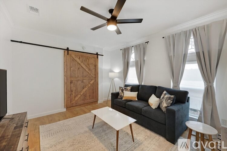 A living room with a black couch, a wooden floor, and a ceiling fan.