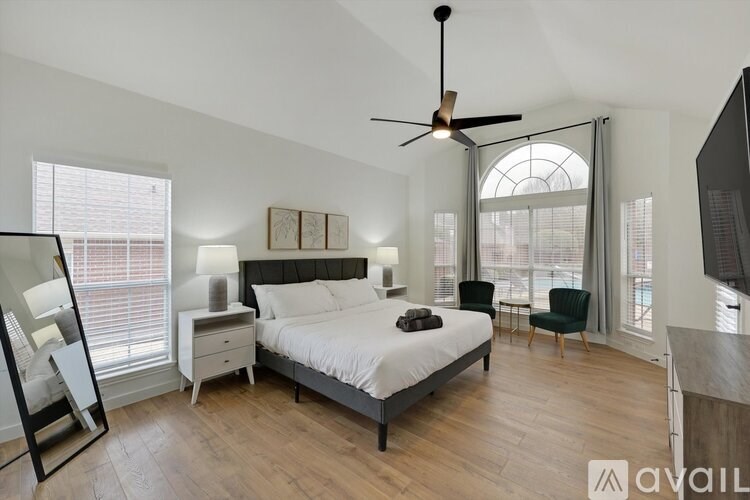 A bedroom with a large bed, a ceiling fan, and a window with blinds.