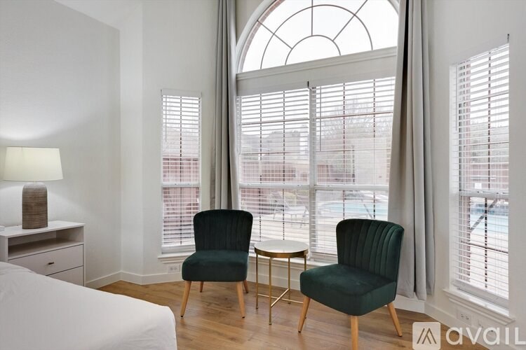 Two green chairs are placed in front of a window with white blinds.