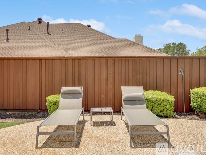 Two lounge chairs are placed on a gravel area in front of a wooden fence.