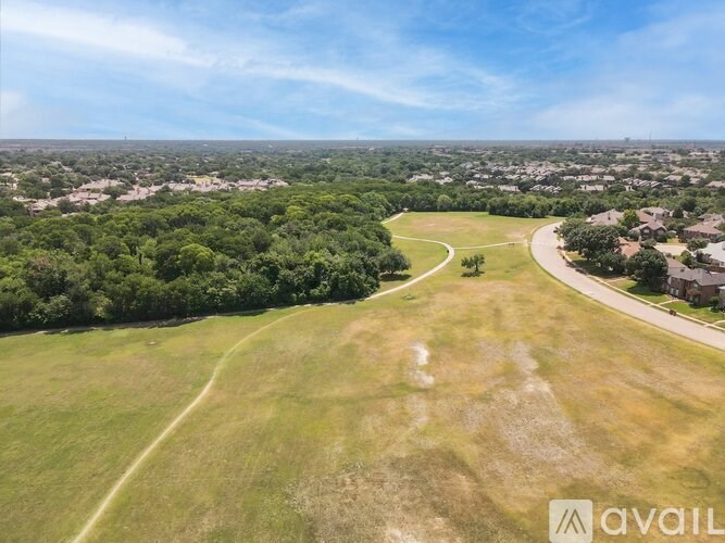 A large open field with a winding path and a residential area in the distance.