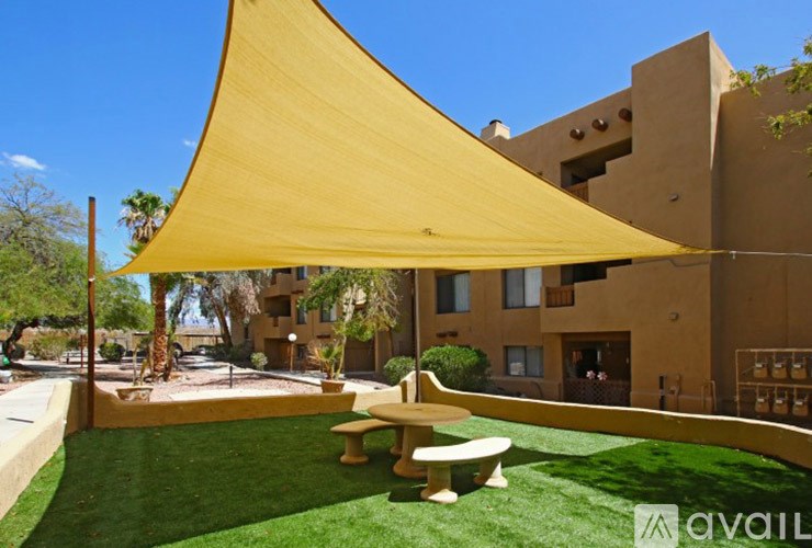 A large yellow shade structure is over a table and chairs outside a building.