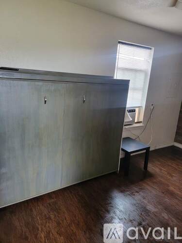 A room with a wooden floor and a grey wall with a cabinet and a small table.