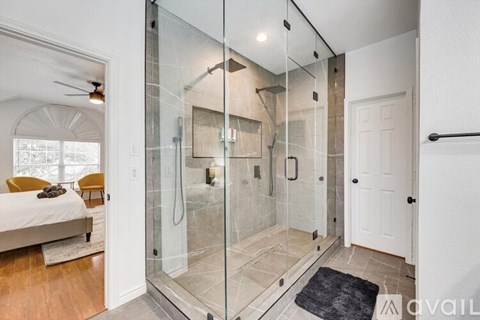 A bathroom with a walk-in shower and a bedroom with a bed and a ceiling fan.