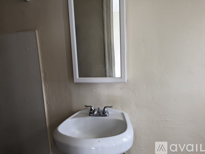 A white sink with a silver faucet is mounted on a wall with a mirror above it.