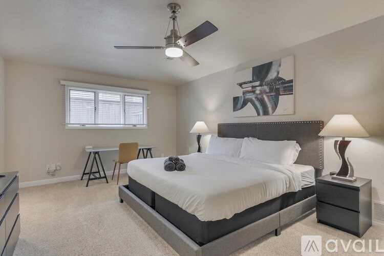 A bedroom with a large bed, a ceiling fan, and a painting on the wall.
