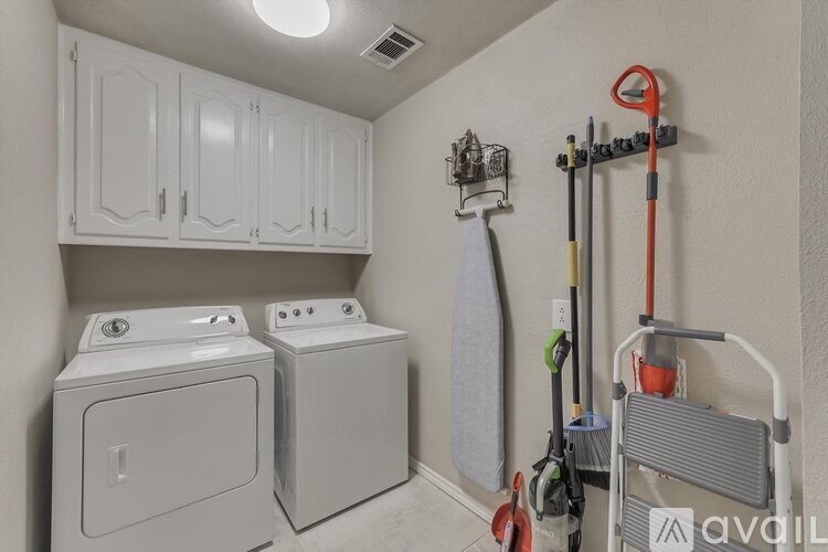 A small laundry room with a washer and dryer, a mop and a broom.