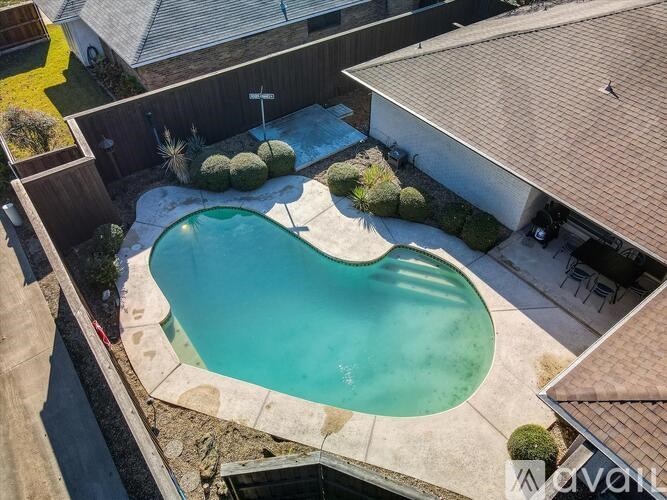 A small kidney-shaped pool surrounded by a concrete patio and a small garden.