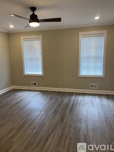 A room with a ceiling fan and two windows.