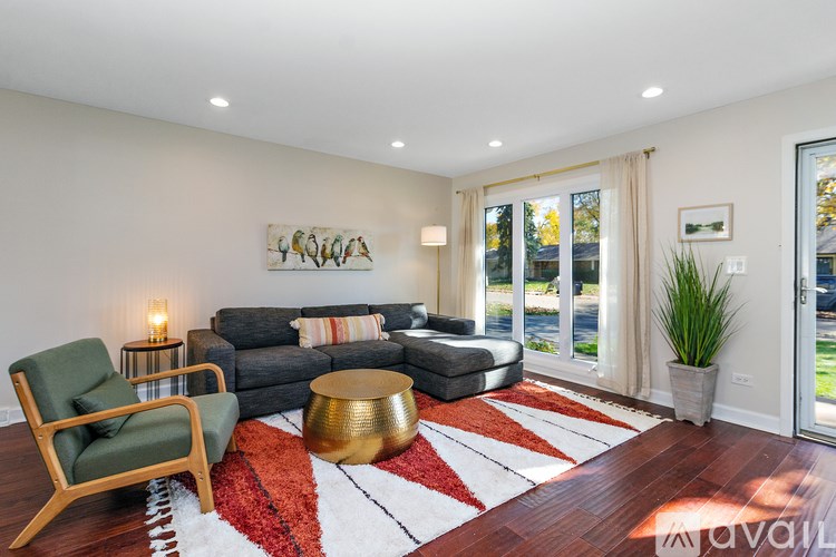 A living room with a green chair, a grey couch, a gold coffee table, and a red and white rug.