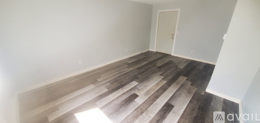 A room with wooden flooring and a white wall with a door on the right side.