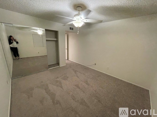 A woman is taking a picture in a room with a carpeted floor and a ceiling fan.