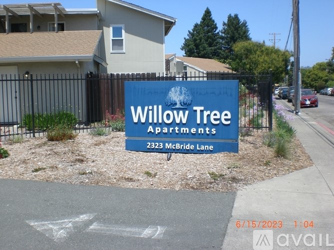 A blue sign for Willow Tree Apartments is in front of a house.