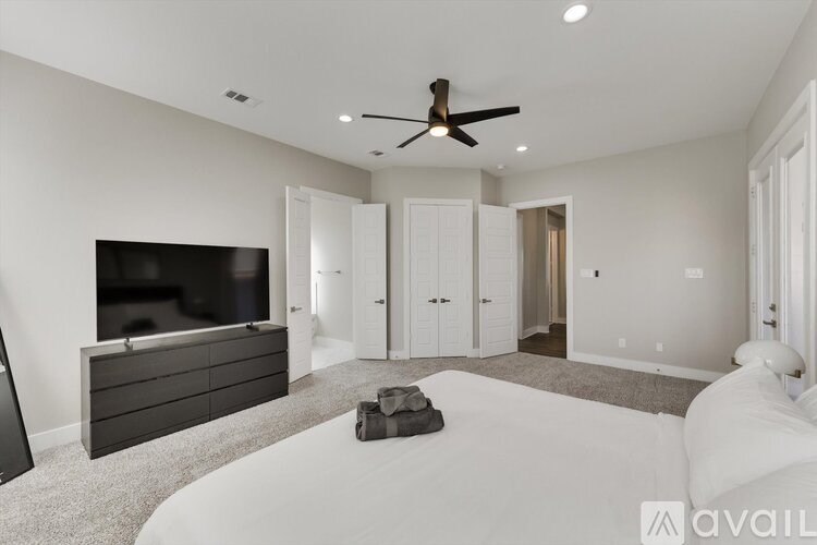 A modern bedroom with a large bed, a flat-screen TV, and a ceiling fan.