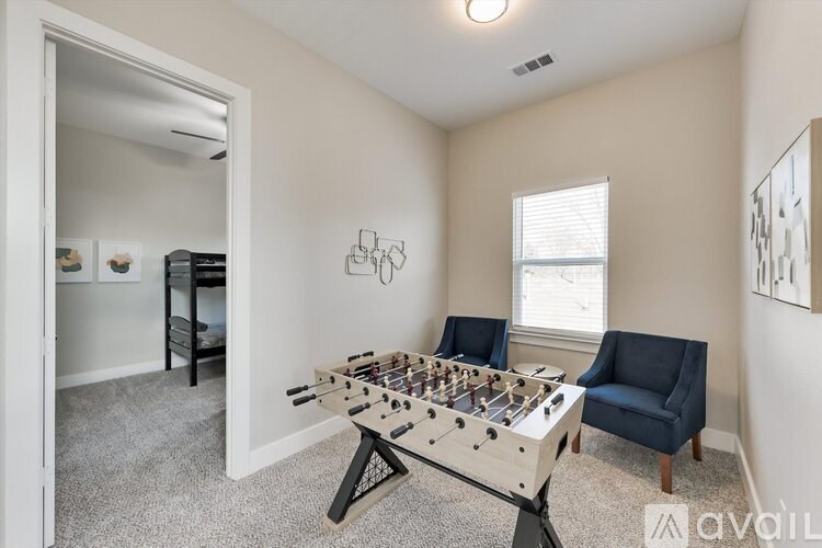 A foosball table sits in the corner of a room with a blue chair and a window.