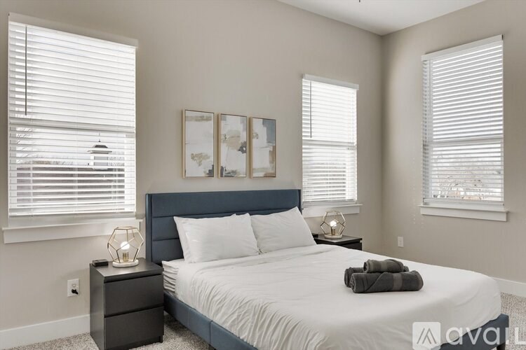 A bedroom with a bed, nightstand, and two windows with blinds.