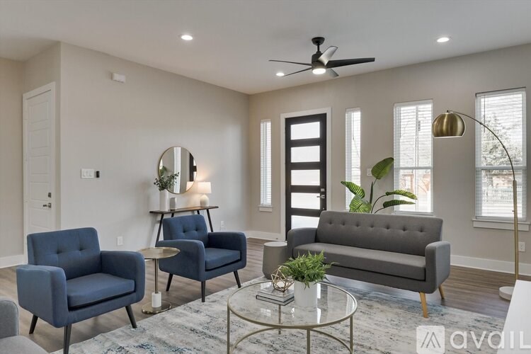 A living room with a grey sofa, two blue armchairs, a glass coffee table, and a ceiling fan.