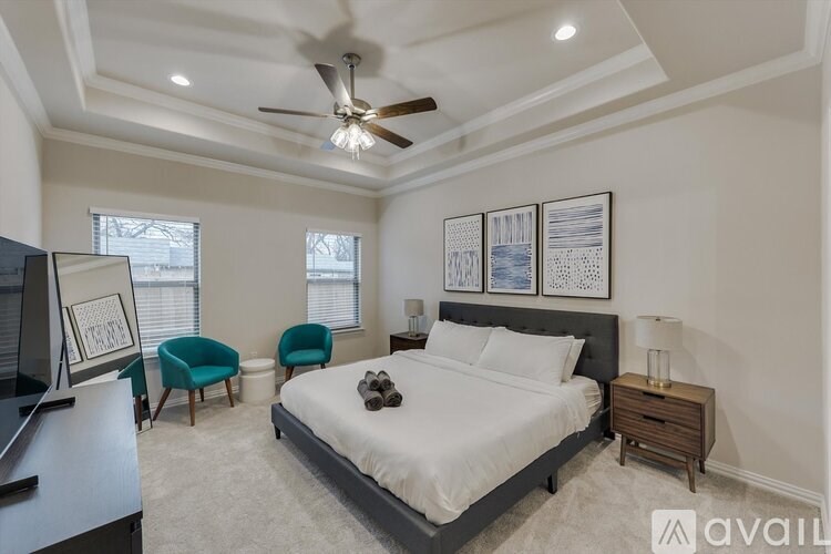 A bedroom with a large bed, a ceiling fan, and two chairs.