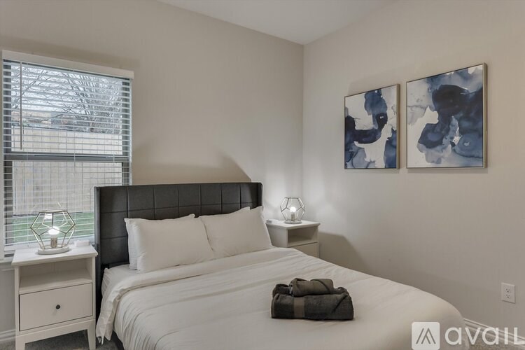 A bedroom with a large bed, a nightstand with a lamp, and two wall-mounted paintings.