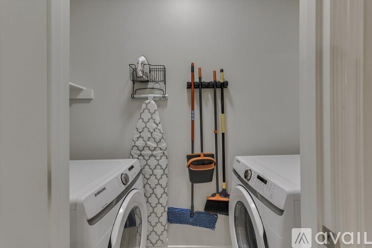 A laundry room with a washer and dryer, a basket on the wall, and a mop and broom leaning against the wall.