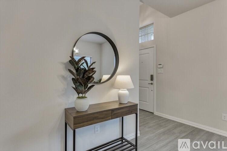A round mirror hangs on a wall above a table with a plant and two lamps.