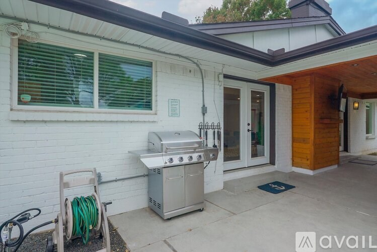 A white house with a grill and a hose on the porch.