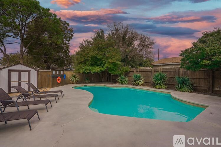 A pool surrounded by a wooden fence and trees with a house in the background.