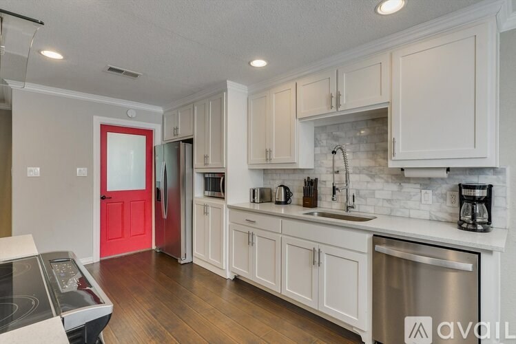A kitchen with white cabinets and a red door.