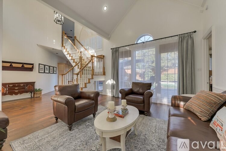 A living room with brown leather furniture and a staircase in the background.