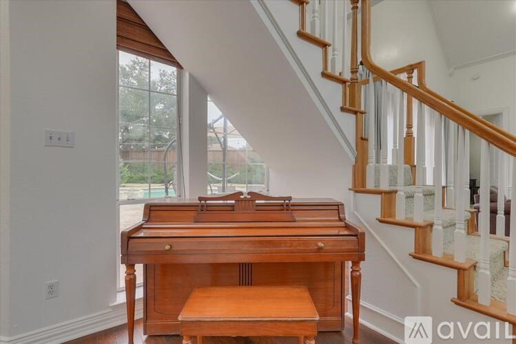 A wooden piano is in a room with a staircase.
