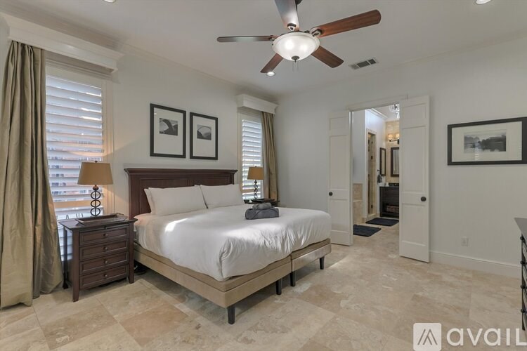 A bedroom with a large bed, a ceiling fan, and a dresser with a lamp on it.