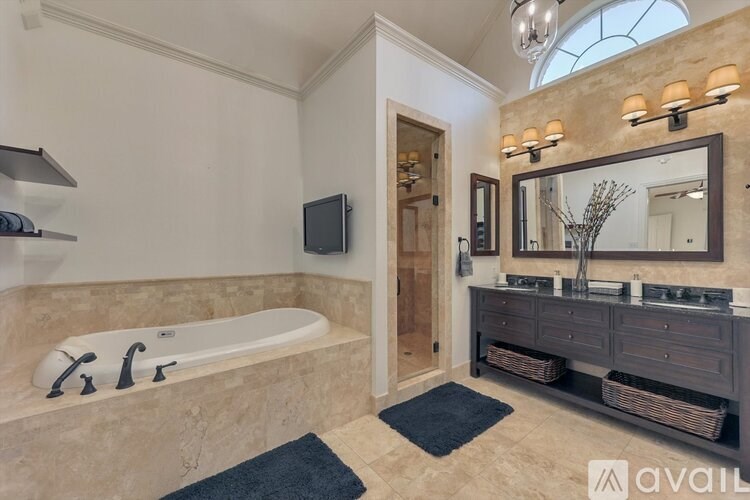 A bathroom with a tub, sink, mirror, and a TV mounted on the wall.