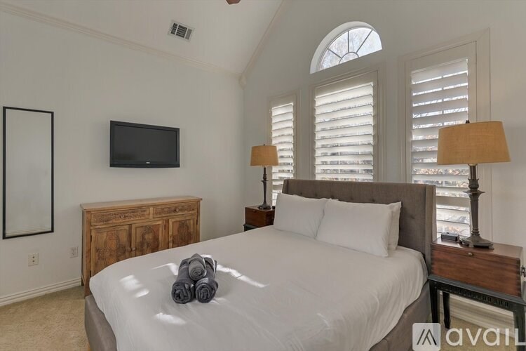 A bedroom with a large bed, a wooden headboard, a flat screen TV, and a window with shutters.
