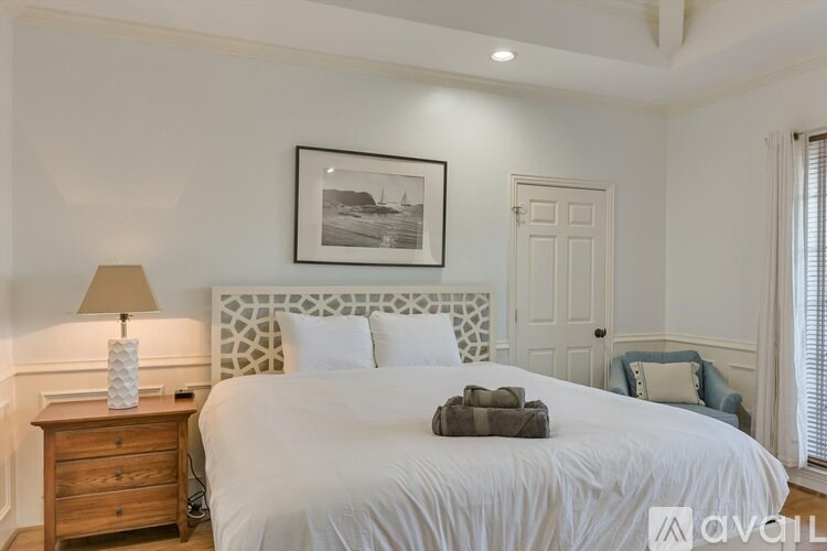 A bedroom with a large bed, a nightstand with a lamp, and a picture on the wall.