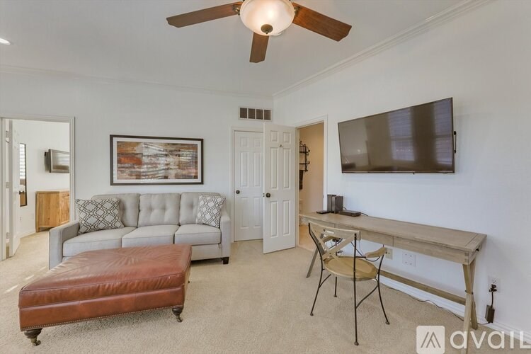 A living room with a grey couch, a brown ottoman, a wooden table, and a television.
